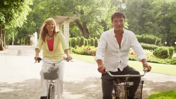 Счастливая взрослая пара катается на велосипедах в парке . — стоковое видео