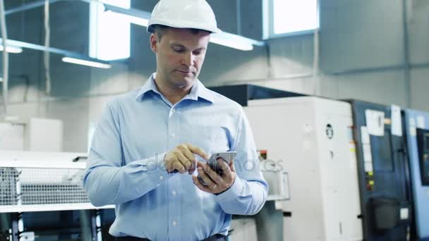 Інженер у капелюсі використовує мобільний телефон на заводі — стокове відео