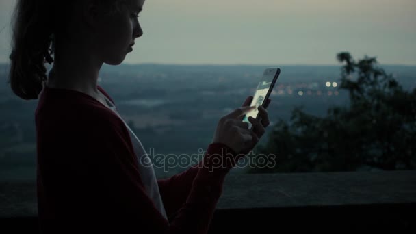 Menina está usando telefone celular ao ar livre à noite — Vídeo de Stock