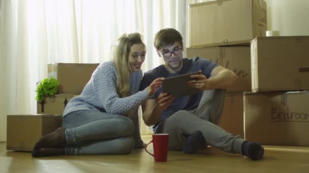 Νεαρό ζευγάρι είναι χρησιμοποιώντας Tablet για ψυχαγωγία σε νέο σπίτι. — Αρχείο Βίντεο