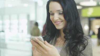 Genç esmer kız güzel mükemmel gülümseme ile cep telefonu kullanarak alışveriş merkezi olduğunu