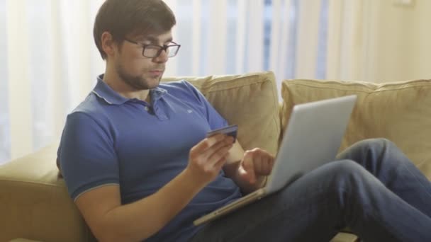 Homem deitado no sofá e usando laptop para compras on-line em casa — Vídeo de Stock