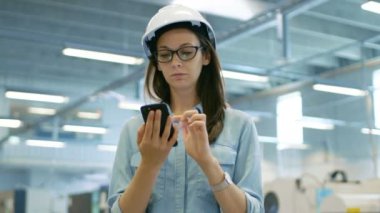 Büyük fabrikada ayakta iken bir sabit Hat kullanan Smartphone içinde kadın mühendis.