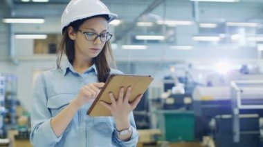 Bir sabit Hat kullanır Tablet bilgisayarda büyük fabrika içinde yürüyüş sırasında kadın mühendis.