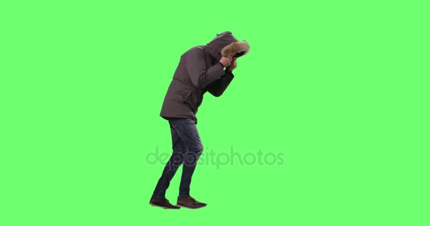 Ο άνθρωπος σε ένα φορώντας χειμερινό μπουφάν με κουκούλα σε περιπάτους κατά του κρύου καιρού και ισχυρό άνεμο. Shot σε μακέτα φόντο πράσινη οθόνη. — Αρχείο Βίντεο