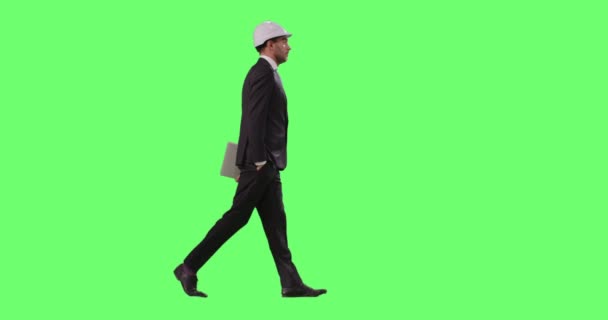 Uomo d'affari con un cappello duro e un vestito sta camminando su un modello di schermo verde sullo sfondo . — Video Stock