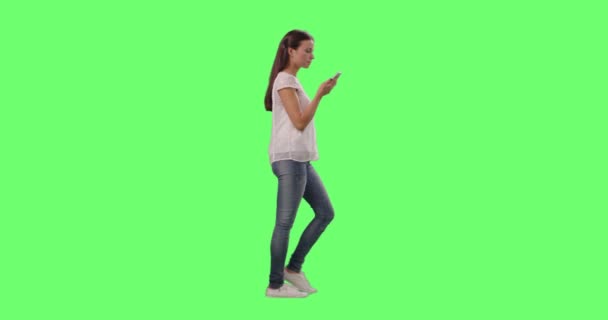 Lässiges junges brünettes Mädchen läuft und spricht auf dem Smartphone auf einem grünen Bildschirm im Hintergrund. — Stockvideo