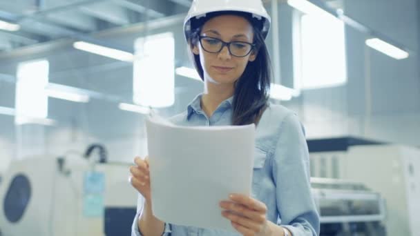 Ingeniera femenina que usa casco duro trabaja con planos mientras está de pie en medio de la gran fábrica . — Vídeos de Stock