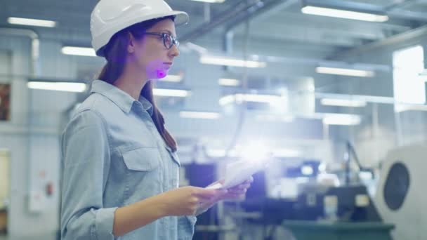Όμορφη μελαχρινή βιομηχανική μηχανικός φορώντας σκληρό καπέλο μελέτες σχεδιαγράμματα και τα έγγραφα, ενώ το περπάτημα μέσα από το εργοστάσιο. — Αρχείο Βίντεο