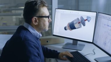 3D türbin üzerinde çalışan üst düzey erkek mühendisi / motor modeli kendi bilgisayarında. Arka planda gördüğümüz büyük fabrika.