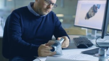 Odaklı erkek Şef Mühendis bileşenin dayanıklılık olup olmadığını denetler. Endüstriyel tasarım yazılımı açık olduğunu onun masaüstü bilgisayar üzerinde. Arka plan büyük fabrikada görülür.