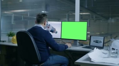 Şef erkek mühendis tasarımlar 3d türbin / motoru büyük bir sanayi şirketi için yaptığı ikinci ekran Mock-up yeşil ekran bilgisayar gösterir. Ofis pencere büyük fabrika dışında görülür.