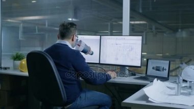 3d modeli bir türbin veya motor bölümü bir şef erkek mühendis tasarımlar. İkinci ekran teknik planları gösterir. Ofis pencere büyük fabrika dışında görülür.