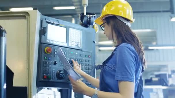 Professional Female Operator in Hard Hat Setting up/ Programming CNC Machine with Help of Control Panel. Big Industrial Factory is Visible. — Stock Video