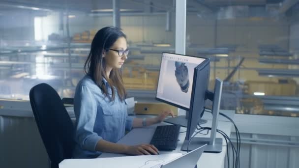 Ingénieur industriel féminin travaille sur son ordinateur avec le logiciel CAD 3D. L'intérieur de l'usine est vu de sa fenêtre de bureau . — Video