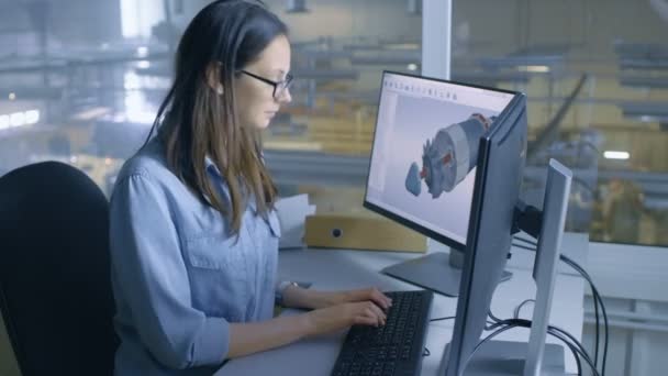 Female Industrial Engineer Works on 3D Turbine/Engine Model in CAD Software on Her Desktop Computer. Inside of the Factory is Seen From Her Office Window. — Stock Video