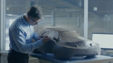 Gri saçlı otomotiv tasarımcısı futuristik araba modeli hamuru Clay tel ile Sculpts. O bir büyük araba fabrikasında bulunan özel bir stüdyoda çalışıyor.