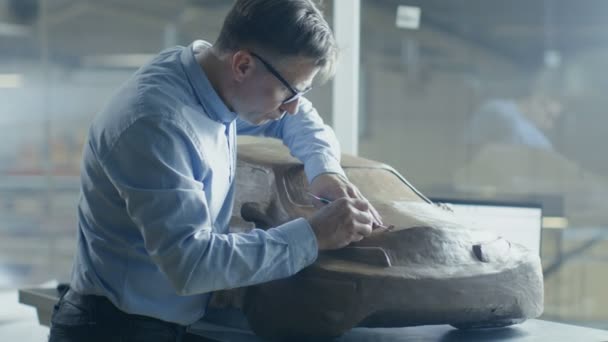 Professionele Automotive ontwerper met Rake beeldhouwt futuristische automodel uit Plasticine klei. Hij werkt in een speciale Studio gelegen In een grote autofabriek. — Stockvideo