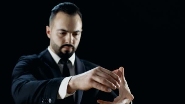 Close-up of a Professional Magician in a Black Suit Performing Card Trick. Throwing and Catching Cards Deck in the Air. Background is Black. — Stock Video