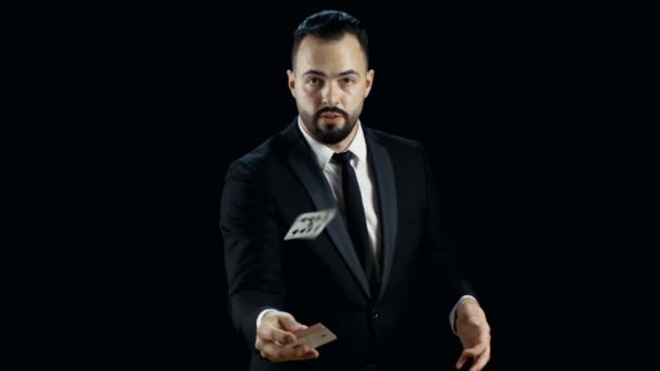 Ein professioneller Magier im dunklen Anzug wirft eine Karte des Kartenspiels in die Kamera. Hintergrund ist schwarz. Zeitlupe. — Stockvideo