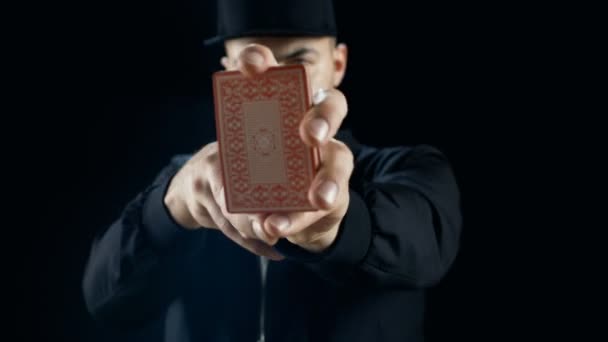Mago callejero profesional en una gorra realiza trucos de cartas de mano. El fondo es negro . — Vídeos de Stock