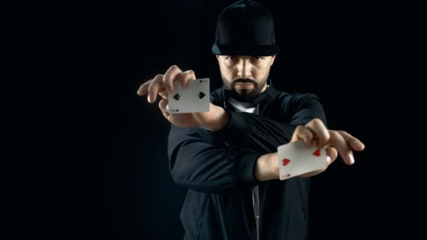 Profesional Street Magician in a Cap lleva a cabo impresionante truco de la mano de la tarjeta. El fondo es negro . — Vídeo de stock