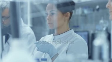 Takım araştırma bilim adamları çalışma ile mikroskop, Yardımcısı geçer örnekleri ile bir şefe bilim adamı ve o görünüyor, onları mikroskop altında slaytlar. Onlar iş Modern bir laboratuvar / Tıp Merkezi.