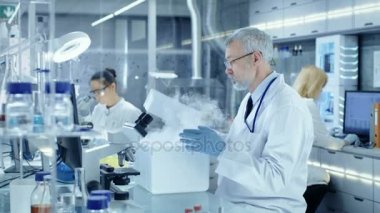 Kıdemli tıbbi araştırma bilim adamı açar buzdolabı kutusu duman geliyor bunun dışında. O meşgul bir Modern laboratuvar merkezinde çalışıyor.