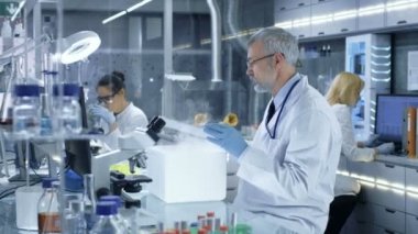 Üst düzey tıbbi araştırma bilim adamı açar buzdolabı kutusu Petri kabına örnekleri ve Examines ile dışarı bu alır. O meşgul bir Modern laboratuvar merkezinde çalışıyor.