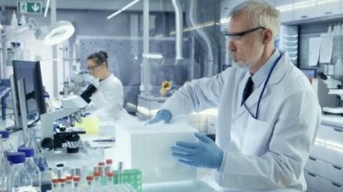 Üst düzey tıbbi araştırma bilim adamı açar buzdolabı kutusu Petri kabına örnekleri ve Examines ile dışarı bu alır. O meşgul bir Modern laboratuvar merkezinde çalışıyor.