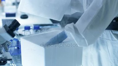 Tıbbi Viroloji araştırma bilim adamı bir Hazmat uygun maske ile çalışır, tüp ile izole virüs dize buzdolabı kutusunda olup olmadığını denetler. O bir steril yüksek teknoloji laboratuarında çalışıyor / araştırma tesisi.
