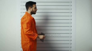 Bir polis istasyonunda tutuklandı adam adımlar ve yan, ön görünüm Mugshot alır. O bir tutuklum turuncu tulum ve Beklemeler tasarlamak. Arka plan grafikte yükseklik.