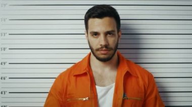 Bir karakol içinde Mugshot için poz adam tutuklandı. O bir tutuklum turuncu tulum ve Beklemeler tasarlamak. Arka plan grafikte yükseklik.