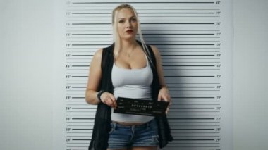 Bir polis istasyonunda tutuklanan kadın adımlar ve yan, ön görünüm vesikalık alır. O şımarık giysiler giyiyor ağır makyaj ve tutar tasarlamak. Arka plan grafikte yükseklik.