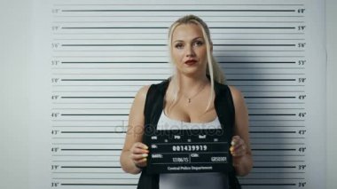 Bir polis istasyonunda tutuklanan kadın adımlar ve yan, ön görünüm vesikalık alır. O şımarık giysiler giyiyor ağır makyaj ve tutar tasarlamak. Arka plan grafikte yükseklik.