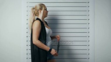 Bir polis istasyonunda tutuklanan kadın adımlar ve yan, ön görünüm vesikalık alır. O şımarık giysiler giyiyor ağır makyaj ve tutar tasarlamak. Arka plan grafikte yükseklik.