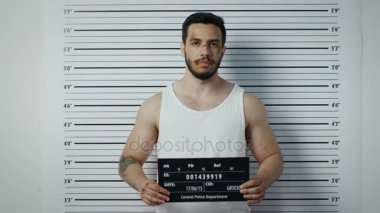 Bir polis karakoluna gittiği adam pozlar yan, ön görünüm Mugshot için tutuklandı. Singlet giyer, o ağır morluk ve afiş tutar. Arka plan grafikte yükseklik.