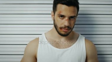 Bir polis karakoluna gittiği adam pozlar yan, ön görünüm Mugshot için tutuklandı. Singlet giyer, o ağır morluk ve afiş tutar. Arka plan grafikte yükseklik.