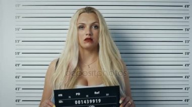 Polis karakolunda tarafı için açık manzaralı Mugshot poz kadın tutuklandı. O çiğnemek sakız, giyer şımarık giyim, ağır makyaj lekeli, saçları darmadağınık ve o afiş tutar. Arka plan grafikte yükseklik.