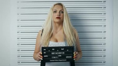 Polis karakolunda tarafı için açık manzaralı Mugshot poz kadın tutuklandı. O çiğnemek sakız, giyer şımarık giyim, ağır makyaj lekeli, saçları darmadağınık ve o afiş tutar. Arka plan grafikte yükseklik.