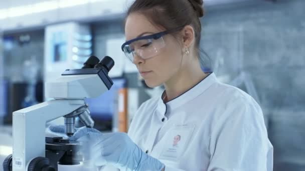 Medical Research Scientists putting Slides in Place and Looking at Samples Under Microscope (en inglés). Trabaja en un laboratorio moderno y brillante . — Vídeos de Stock