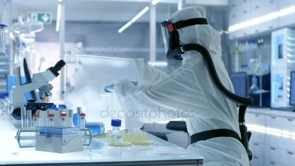 Ιατρική ιολογία επιστήμονας ερευνητικές εργασίες σε Hazmat κοστούμι με μάσκα, παίρνει έξω τα σωληνάρια από ψυγείο κουτί. Εργάζεται σε ένα εργαστήριο αποστειρωμένων υψηλής τεχνολογίας, ερευνητικές εγκαταστάσεις. — Αρχείο Βίντεο