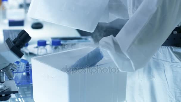 El científico de la investigación de la virología médica trabaja en un traje de la estera de peligro con la máscara, inspecciona el tubo de prueba con la secuencia aislada del virus de la caja del refrigerador. Trabaja en un laboratorio estéril de alta tecnología / centro de investigación . — Vídeos de Stock