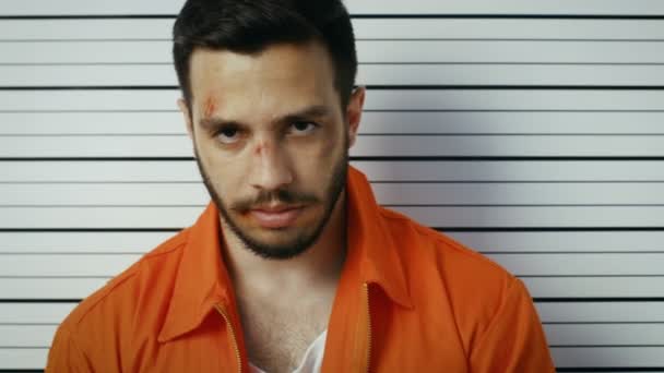 在警察局逮捕小伙侧前, 视图的面部照片。他是穿着囚犯桔红色、 嚼口香糖和持有标语牌。在后台的高度图. — 图库视频影像