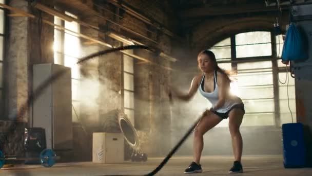 Sportovní žena aktivně v tělocvičně cvičení s bitva lana během její Cross Fitness cvičení / High intenzita intervalový trénink. Ona je sval a zpocené, tělocvična je v opuštěné továrně. — Stock video