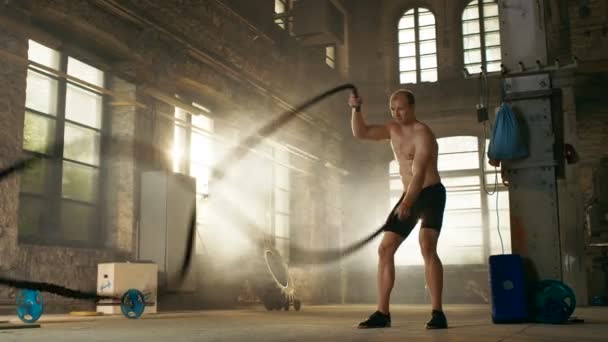 Hombre musculoso sin camisa en un gimnasio hace ejercicios con cuerdas de batalla durante su entrenamiento Cross Fitness / entrenamiento de intervalo de alta intensidad . — Vídeo de stock