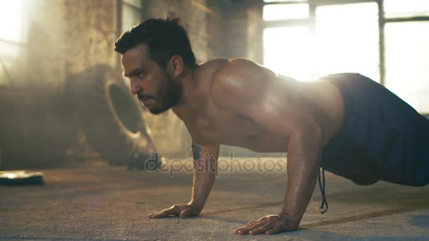 Muscular Shirtless Man met un effort lourd à faire des pompes dans une usine déserte transformée en salle de gym. Une partie de son entraînement de remise en forme croisée / entraînement par intervalles de haute intensité . — Video