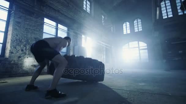 Strong Muscular Man Lifts Tire as Part of His Cross Fitness Routine (en inglés). Está cubierto de sudor y trabaja en una fábrica abandonada remodelada en el gimnasio . — Vídeos de Stock