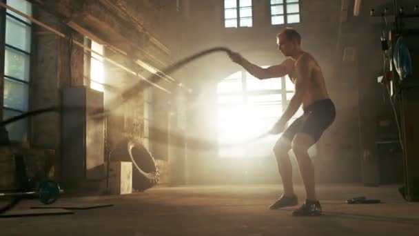 Strong Muscular Shirtless Sportsman trabalha duro com cordas de batalha como parte de sua rotina de treinamento Cross Fitness. Ele está coberto de suor e exercícios em uma fábrica abandonada remodelada no ginásio . — Vídeo de Stock