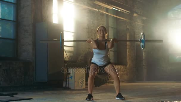 Erős sportos nő sportruházat felvonók nehéz súlyzó és csinál zömök, mint egy része a Her Cross Fitness képzési rutin. Edzőterem található felújított gyári. — Stock videók